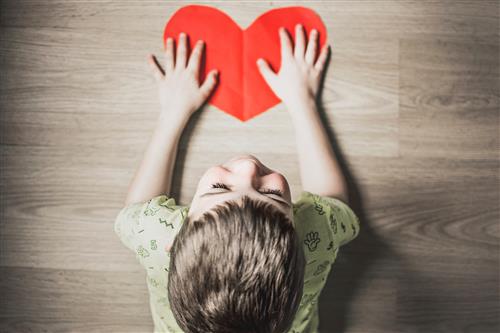 little boy with hands on paper heart 
