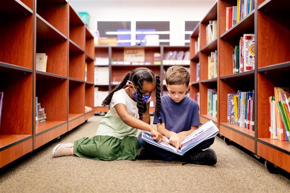 two children on the floor in the library reading a book